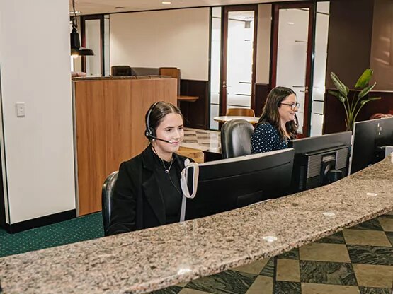 Two Servcorp receptionists wearing headsets are professionally managing calls and client inquiries at a polished front desk