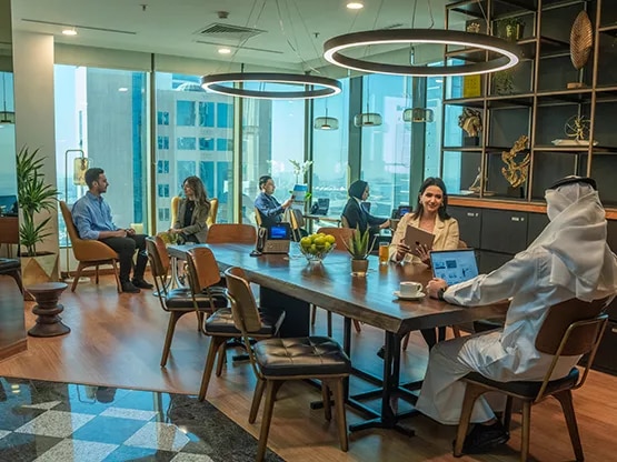  A dynamic shared workspace at Sahab Tower, Kuwait, where professionals collaborate and work individually in a bright, modern setting with large windows offering city views.
