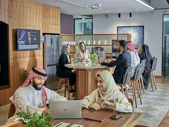 Professionals collaborate and connect in the modern kitchen area at Servcorp Al Akaria Plaza, designed for comfort, networking, and casual business interaction.